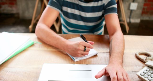 Young man taking notes while working with laptop in office - Download Free Stock Images Pikwizard.com