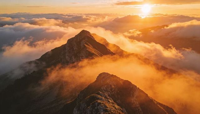 Golden sunrise over jagged alpine ridge rising above vibrant sea of clouds with sunlit mist