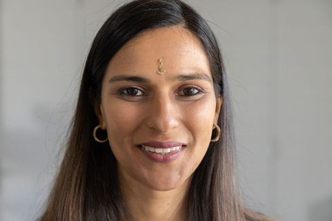 Indian woman smiling with gold bindi and hoop earrings closeup portrait, warm expression