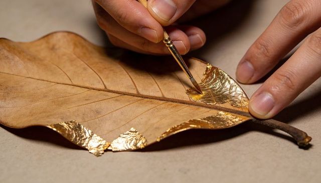 Gilding dried leaf with gold foil using fine brush and artisan hands