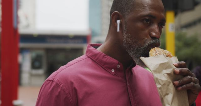 Man Wearing Earbuds Eating Sandwich on City Street - Download Free Stock Images Pikwizard.com