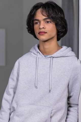 Teen male standing in light gray hoodie wearing thin chain necklace in minimal interior