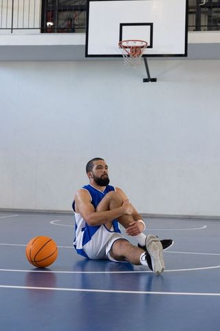 Male basketball player suffering injury on blue indoor court
