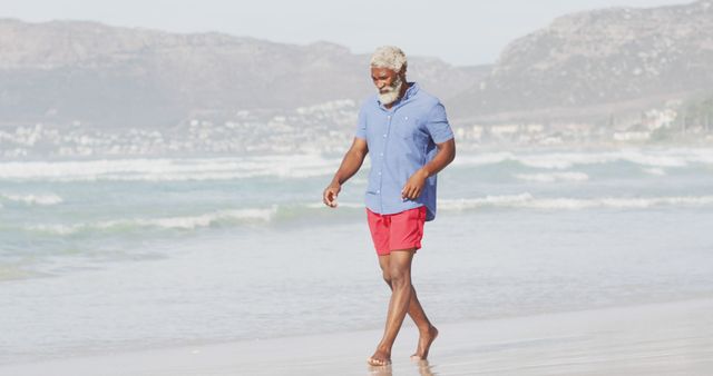 Senior african american man walking alone on sunny beach. healthy and active time beach holiday.
