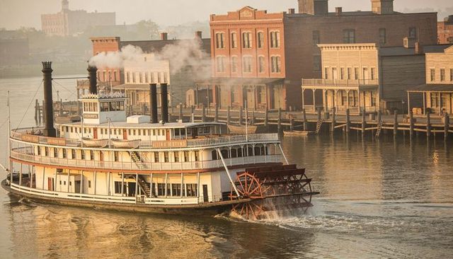 Historic sidewheel paddle steamer gliding on riverfront at golden hour with red paddlewheel