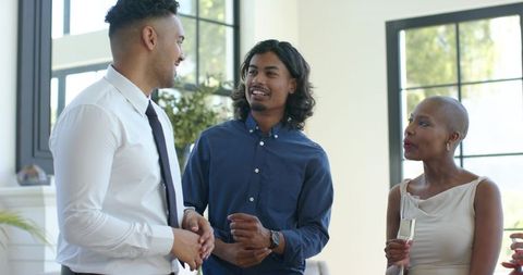 Young professionals networking and chatting in sunlit reception lounge with champagne