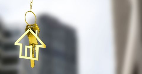 Golden house keychain against blurred cityscape background