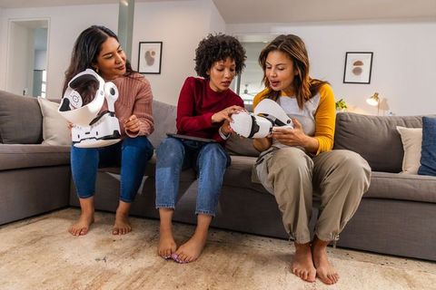 Three women testing wearable robotic devices with tablet in casual living room tech demo
