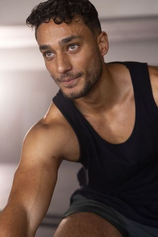 Athletic man stretching forward in gym wearing black tank top and shorts focused training