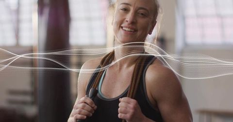 Smiling fit woman holding heavy jump rope around neck after cardio and strength workout