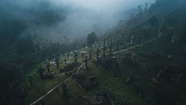 Fog-shrouded hillside cemetery with rows of weathered stone crosses on mossy ridge in mist