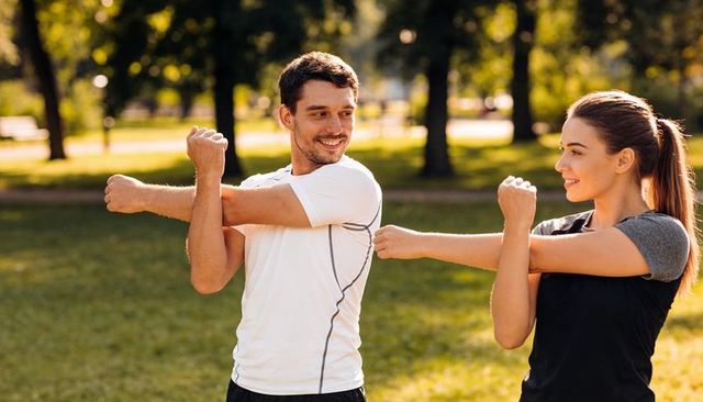 Young couple stretching in sunlit park before outdoor workout, smiling and warming up
