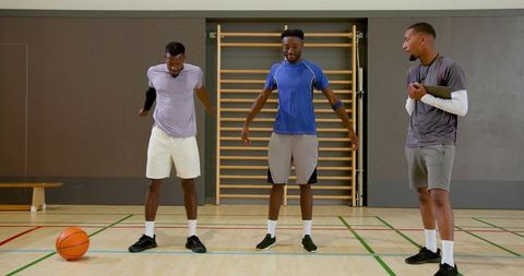 Diverse male teammates warming up on indoor basketball court with coach and ball
