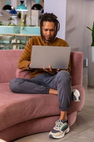 African american man working on laptop on pink sofa in modern coworking lounge