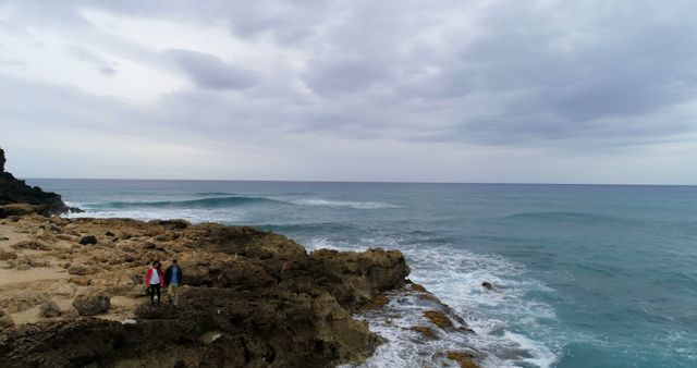 Couple Standing on Rocky Shoreline Looking at Ocean Waves Under Cloudy Sky - Download Free Stock Images Pikwizard.com