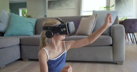 Girl wearing vr headset and headphones reaching forward while playing virtual game at home
