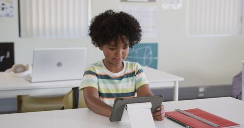 Young student using tablet on stand in classroom wearing striped t-shirt and studying