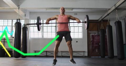 Mid-adult athlete lifting barbell in urban gym with hanging punching bags and neon chart