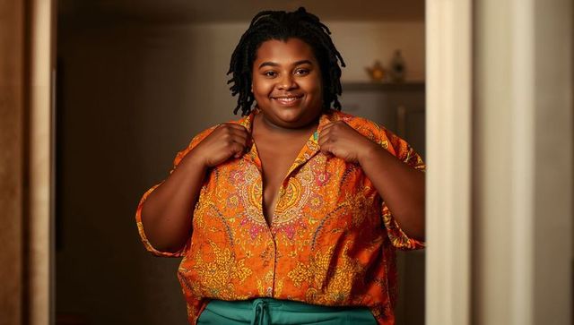 Smiling woman standing in doorway wearing vibrant orange paisley blouse and teal trousers