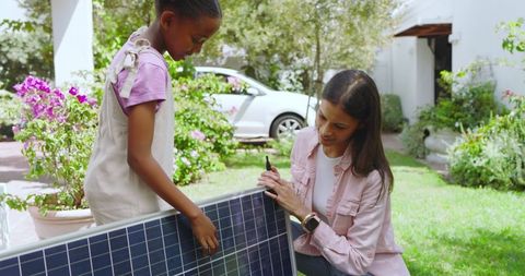 Mother and Daughter Installing Solar Panel in Vibrant Garden