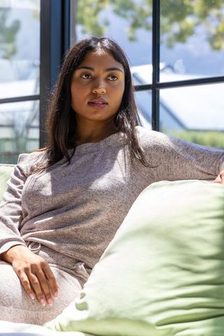 Relaxing woman in knit loungewear on sunlit sofa by black-framed window