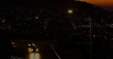 Nighttime Car Lights on Serpentine Road Against City Horizon