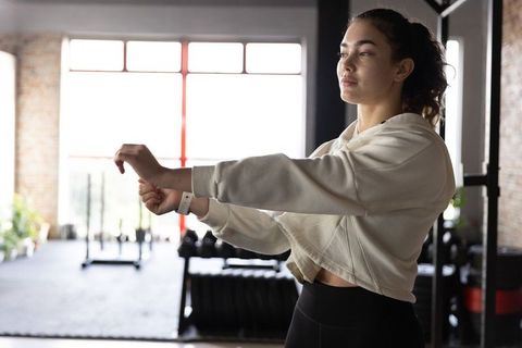 Woman adjusting fitness tracker while stretching in industrial gym with natural light