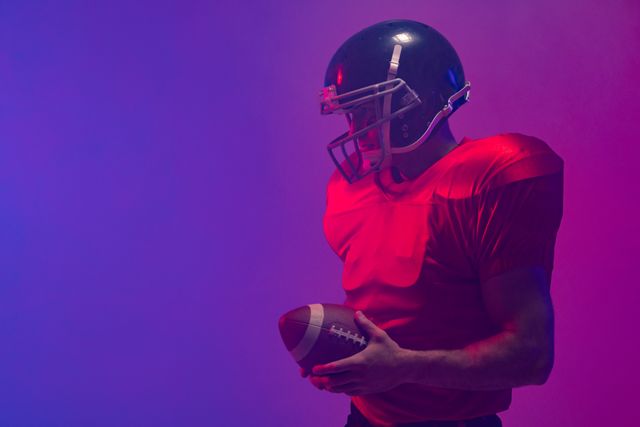 Caucasian male american football player holding ball, in purple and pink light, copy space. Athlete, sport, competition, confidence and fitness concept.
