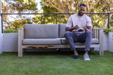 Mature african man cleaning sneaker on balcony sofa, casual footwear care and calm