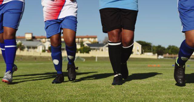 Football players running on a grassy field in colorful uniforms, practicing for a match. Perfect for sports-related websites, athletic training guides, teamwork concepts, youth sports promotion, or fitness blogs.