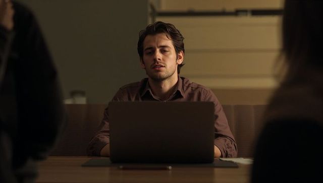 Focused young professional reviewing laptop in dim conference room during meeting