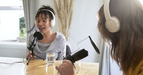 Diverse female cohosts recording in-home podcast with broadcast microphones and headphones