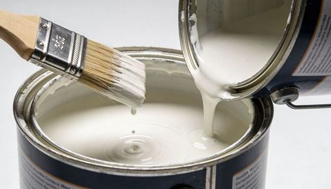 Pouring off-white paint between metal cans with dripping brush closeup for home renovation