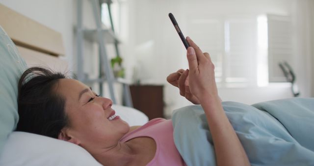 Woman Smiling and Using Smartphone While Lying in Bed - Download Free Stock Images Pikwizard.com