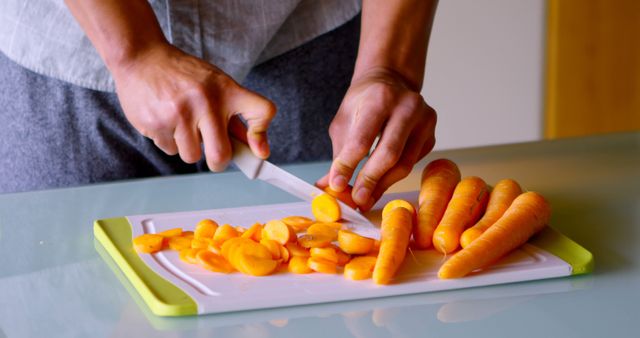 A person is slicing carrots on a cutting board, with copy space. Careful knife skills are demonstrated in the preparation of fresh vegetables for a meal.