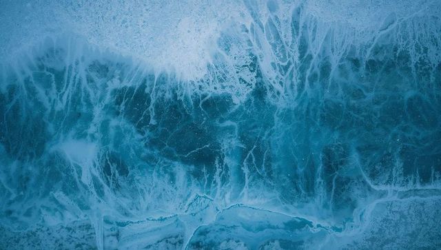 Aerial teal ocean waves crashing and swirling with frothy sea foam and icy textures