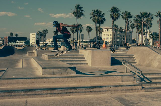 Skateboarder performing tricks and leap in urban skate park surrounded by palm trees and buildings. Exciting skateboarding scene under sunny sky. Perfect for use in sports websites, youth culture promotions, urban lifestyle blogs, and extreme sports posters.