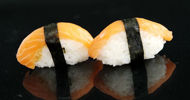 Two pieces of salmon nigiri sushi are presented on a reflective black surface, showcasing the simplicity and elegance of Japanese cuisine. Fresh slices of salmon rest atop small mounds of vinegared rice, bound together by a strip of seaweed, inviting a taste of traditional flavors.