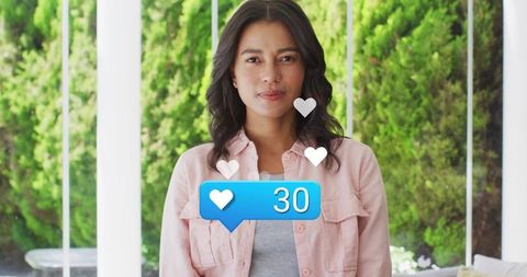 Woman wearing pink shirt receiving social media likes in sunlit home sunroom portrait