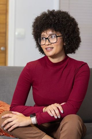 Young curly-haired woman in maroon turtleneck on sofa wearing glasses and smartwatch