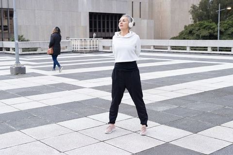 Mature woman standing confidently in urban plaza wearing headphones and casual activewear