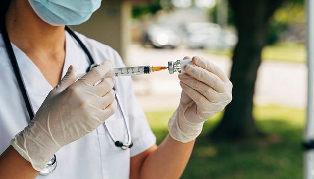 Nurse preparing vaccine syringe outdoors wearing gloves, mask and stethoscope