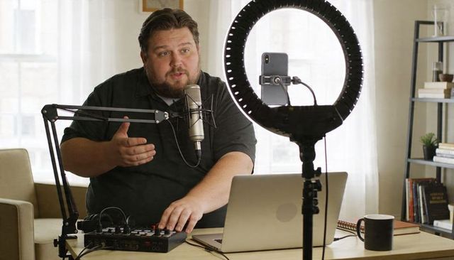 Podcast creator recording in home studio with ring light, condenser microphone and laptop