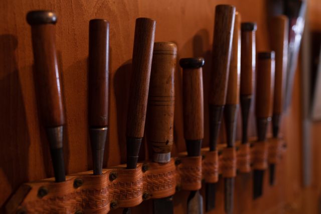Close up view of a row of chisels belonging to a luthier in a workshop, part of the tools of their trade, hanging on the wall in the sunlight.