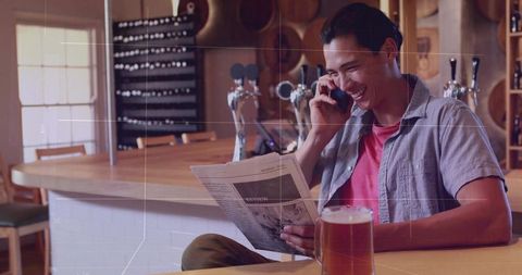 Casual patron reading newspaper and talking on phone in warm craft brewery