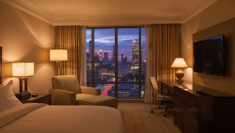Luxury hotel room with floor-to-ceiling window overlooking city skyline at dusk