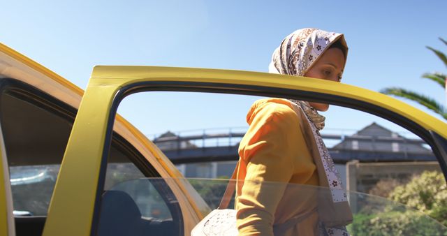 Front view of a young biracial woman wearing a hijab, getting out of a taxi in a city
