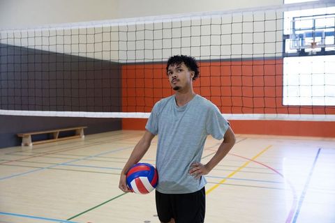 Young athlete standing with volleyball under net in indoor gymnasium preparing serve