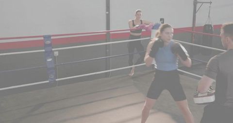 Female boxer sparring with coach doing mitt work in boxing ring during training session