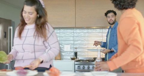 Diverse friends preparing meal together in bright contemporary kitchen